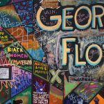 A colorful wall memorial dedicated to George Floyd has different phrases written across it in different people's handwritings with phrases such as "Black Women Matter" and "8 minutes, 46 seconds"